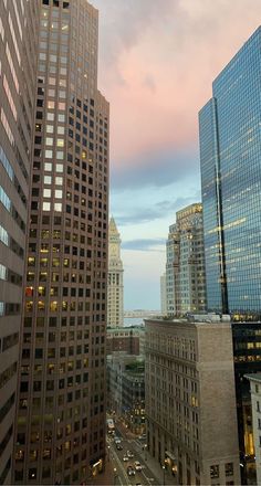 the city is full of tall buildings and skyscrapers at dusk, with cars driving on the street below