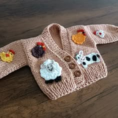 a knitted cardigan with farm animals on the front and sides, sitting on a wooden surface