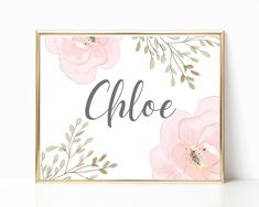 a pink and gold floral name sign on a white wall