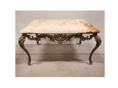 a marble top coffee table with metal legs and scroll work on the base, in an antique style