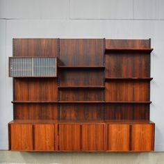 a wooden bookcase sitting on top of a cement floor next to a white wall