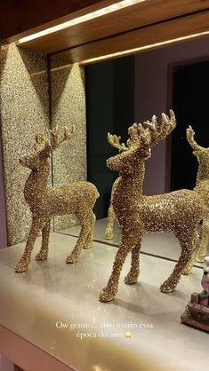 three gold reindeer statues sitting on top of a white counter next to a mirror in a room