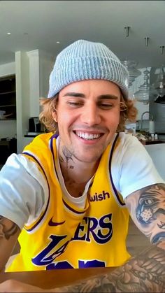 a man with tattoos and a beanie smiles at the camera while wearing a lakers jersey