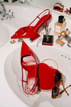 a pair of red high heeled shoes sitting on top of a sink next to sunglasses