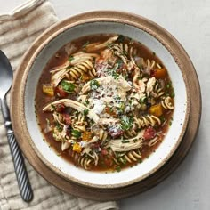 a bowl filled with pasta and vegetables on top of a cloth next to a spoon