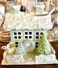 a small white house sitting on top of a wooden table next to a glass vase