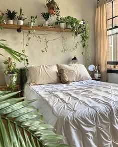 there is a bed with white sheets and plants on the headboard