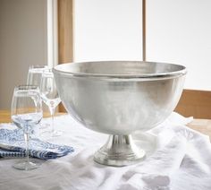 a silver bowl sitting on top of a table next to wine glasses and napkins