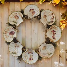 a wreath made out of seashells on top of a wooden fence with leaves around it