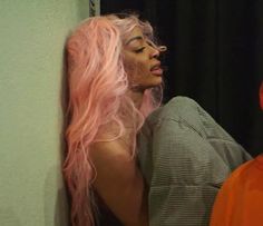 a woman with pink hair is leaning against a wall next to an orange plastic man