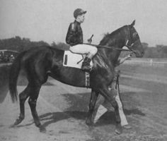 a woman riding on the back of a horse down a race track in black and white