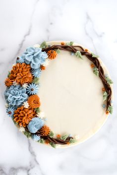 a cake decorated with blue and orange flowers on a marble countertop in the shape of a circle