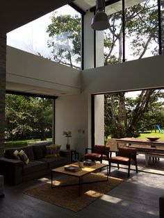 a living room with couches and tables in front of large windows overlooking the trees