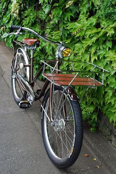 a bike parked next to a bush with green leaves on it's sides and a wooden seat