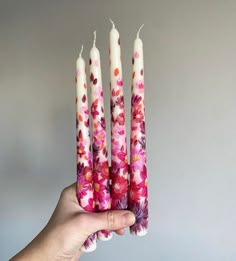 a hand holding three candles with pink flowers on them and one white candle in the middle