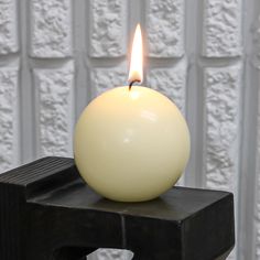 a white candle sitting on top of a black object in front of a white wall