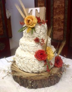 a three tiered wedding cake decorated with flowers and wheat on a tablecloth covered table