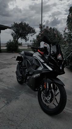 a black motorcycle parked in a parking lot next to some trees and bushes on a cloudy day