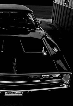 a black and white photo of a muscle car parked in a parking lot next to a building