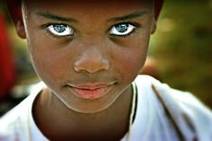 a close up of a child wearing a hat with blue eyes and a white shirt