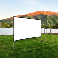 an outdoor movie screen in the grass with mountains in the backgrouds behind it