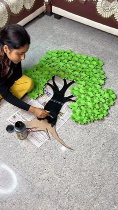 a woman sitting on the floor working on a tree made out of newspaper paper and scissors