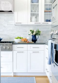 a white kitchen with stainless steel appliances and blue rugs on the hardwood flooring