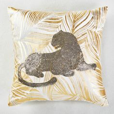 a gold and white pillow with a lion on it's back, surrounded by palm leaves