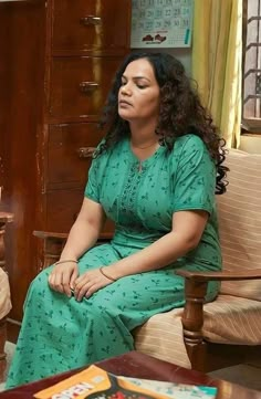 a woman in a green dress sitting on a couch next to a table with books