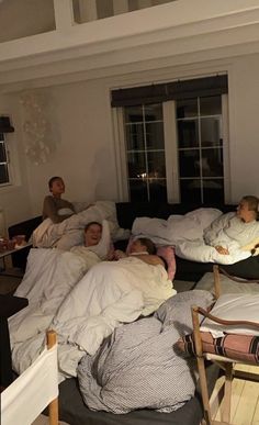 a group of people sleeping on top of pillows in a room with windows and furniture