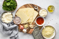 the ingredients to make an appetizer laid out on a cutting board, including parmesan cheese and spinach leaves