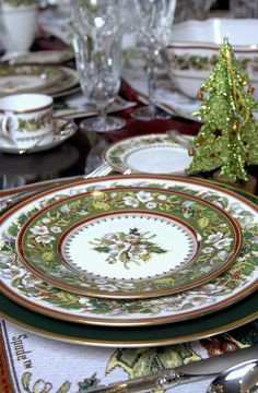 the table is set for christmas dinner with plates, silverware and green napkins