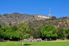 the hollywood sign is on top of a hill in front of trees and people walking around