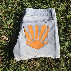 a pair of blue jeans with an orange sun patch on the side sitting in grass