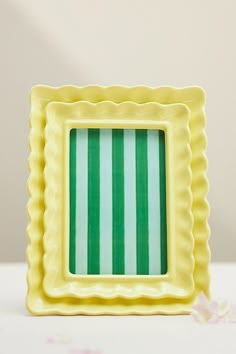 a small yellow and green square shaped object on a white surface with flowers in the background