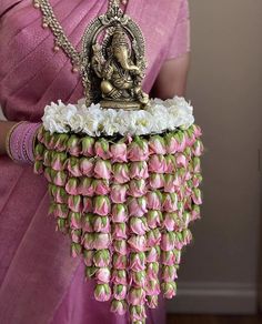 a woman in a pink saree holding a small statue made out of flowers and leaves