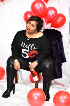 a woman sitting on a chair with balloons around her and a bottle of wine in front of her