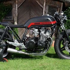 a black and red motorcycle parked on top of a lush green field next to a wooden building