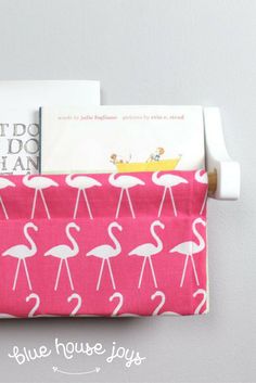 a pink flamingo print toilet paper roll holder with two books on it and a yellow boat in the background