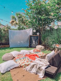 an outdoor area with blankets and pillows on the grass, next to a chalkboard sign