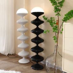 three tall black and white lamps next to a vase with a plant in it on the floor