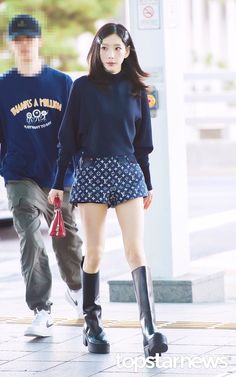 a man and woman walking down the street together wearing black boots, blue sweater and patterned shorts