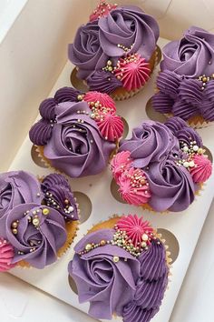 cupcakes with purple frosting and pink flowers in a box