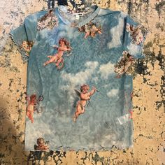 the shirt has cherubs on it and is blue with white clouds in the background