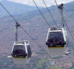 two gondolas with people riding on them in the sky above a city and mountains