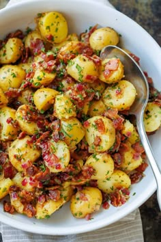 a white bowl filled with potatoes covered in bacon and topped with parsley next to a spoon