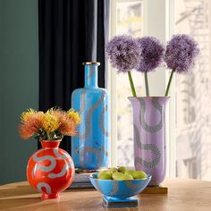 three vases with flowers in them sitting on a table next to fruit and vegetables