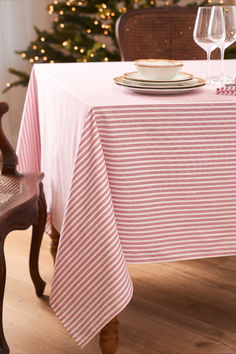 a table with a pink and white striped cloth on it, next to a christmas tree