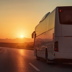 a white bus driving down the road at sunset or sunrise with mountains in the background