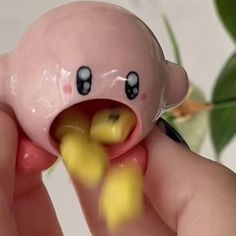 a hand holding a pink toy with black eyes and yellow rubber ducky in it's mouth